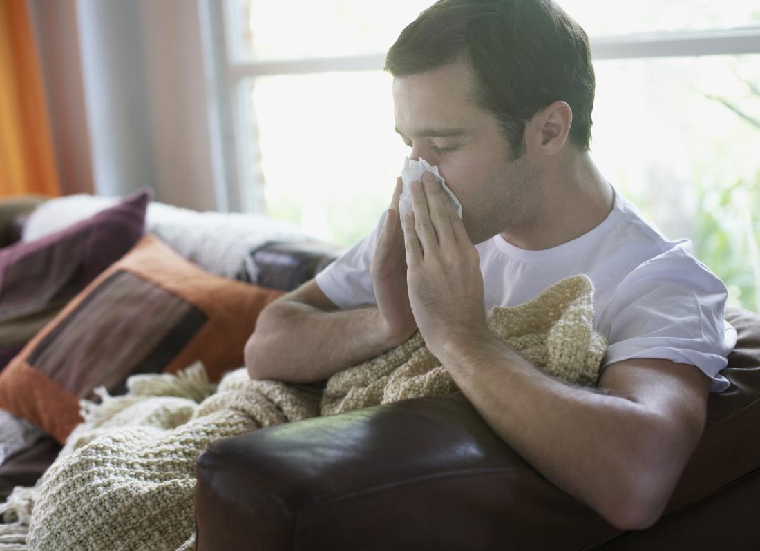 man sitting on a sofa blowing his nose