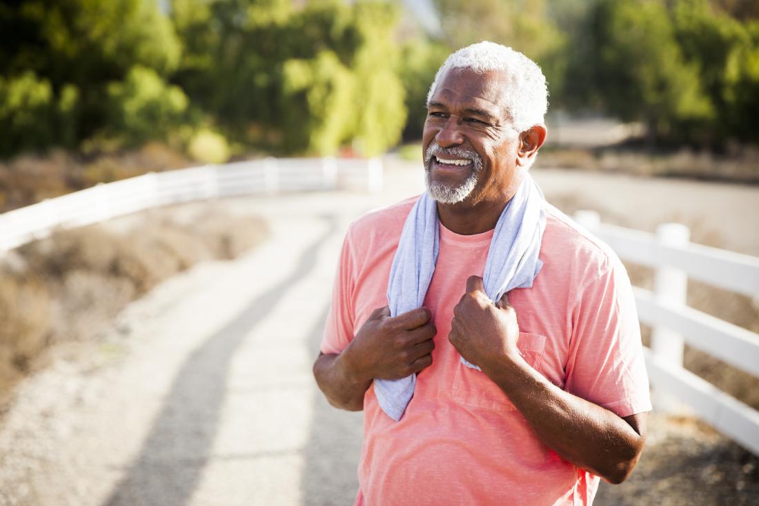 Older man stands outdoors with towel around his neck after exercise