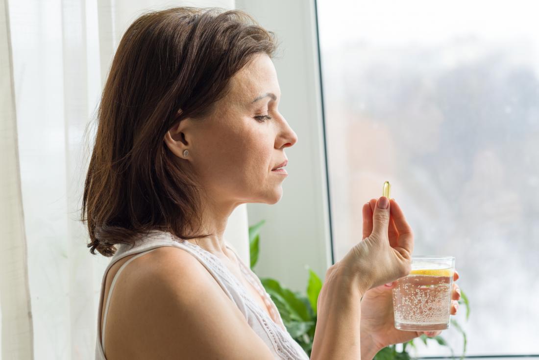 Woman taking dietary supplement with glass of water.