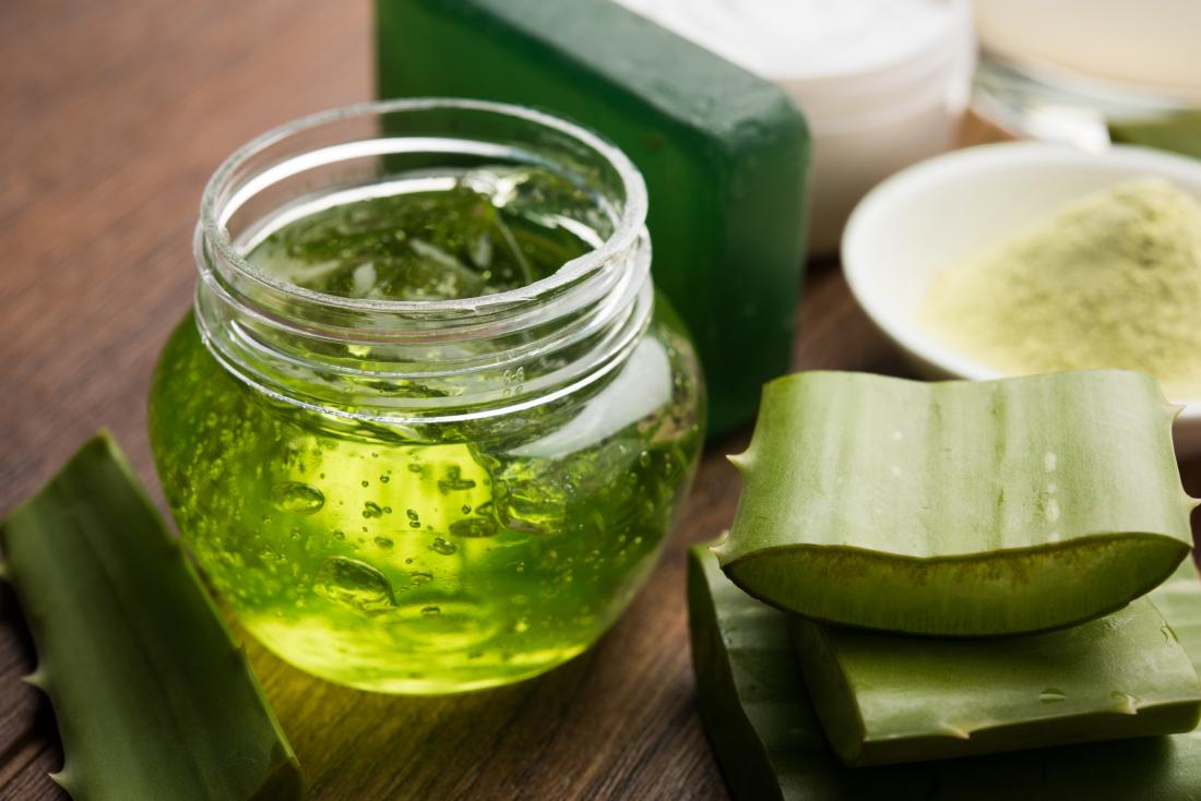 Aloe vera gel in glass pot with cut up plant next to it on wooden table