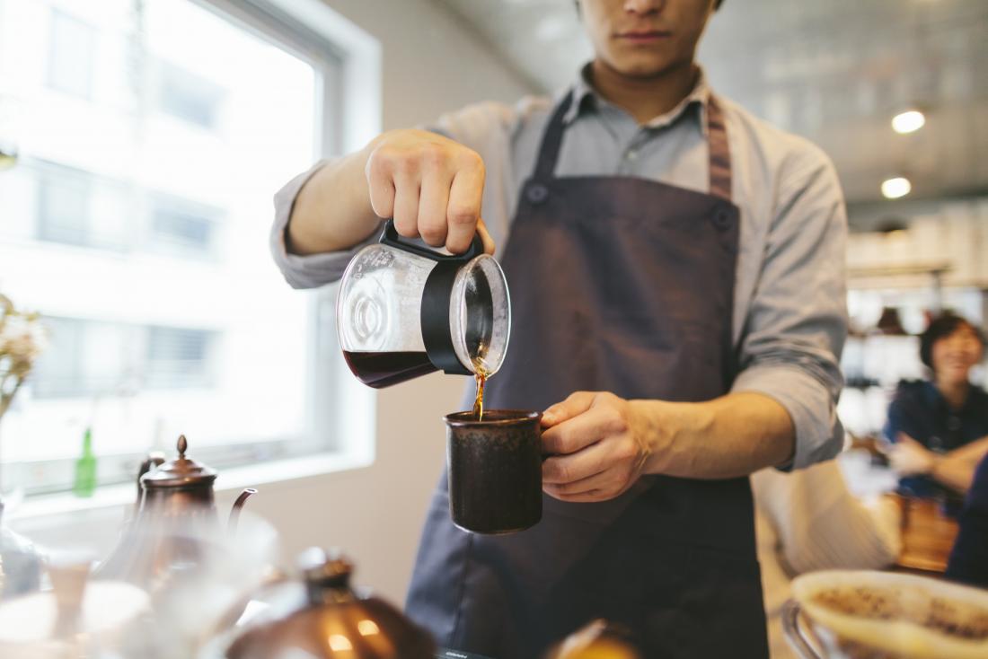 Barista pouring caffeinated coffee into mug in cafe