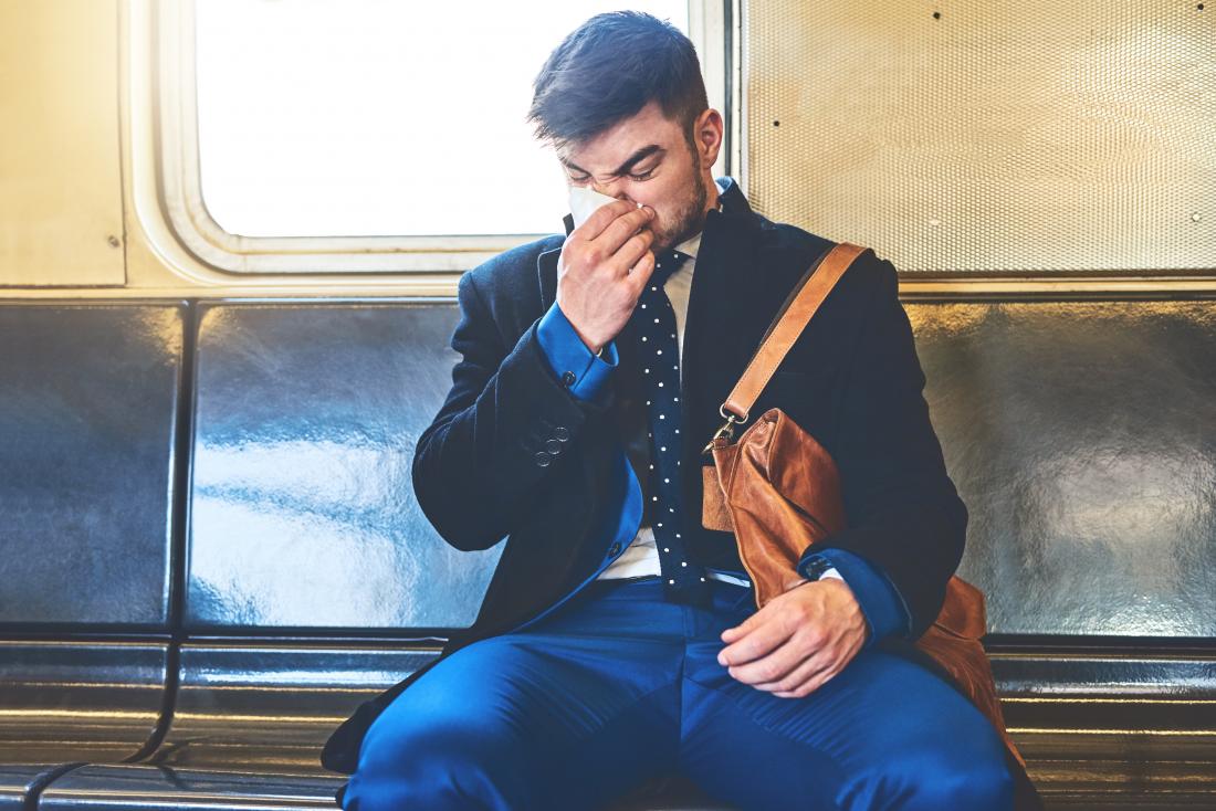 Man sitting on train blowing nose into tissue
