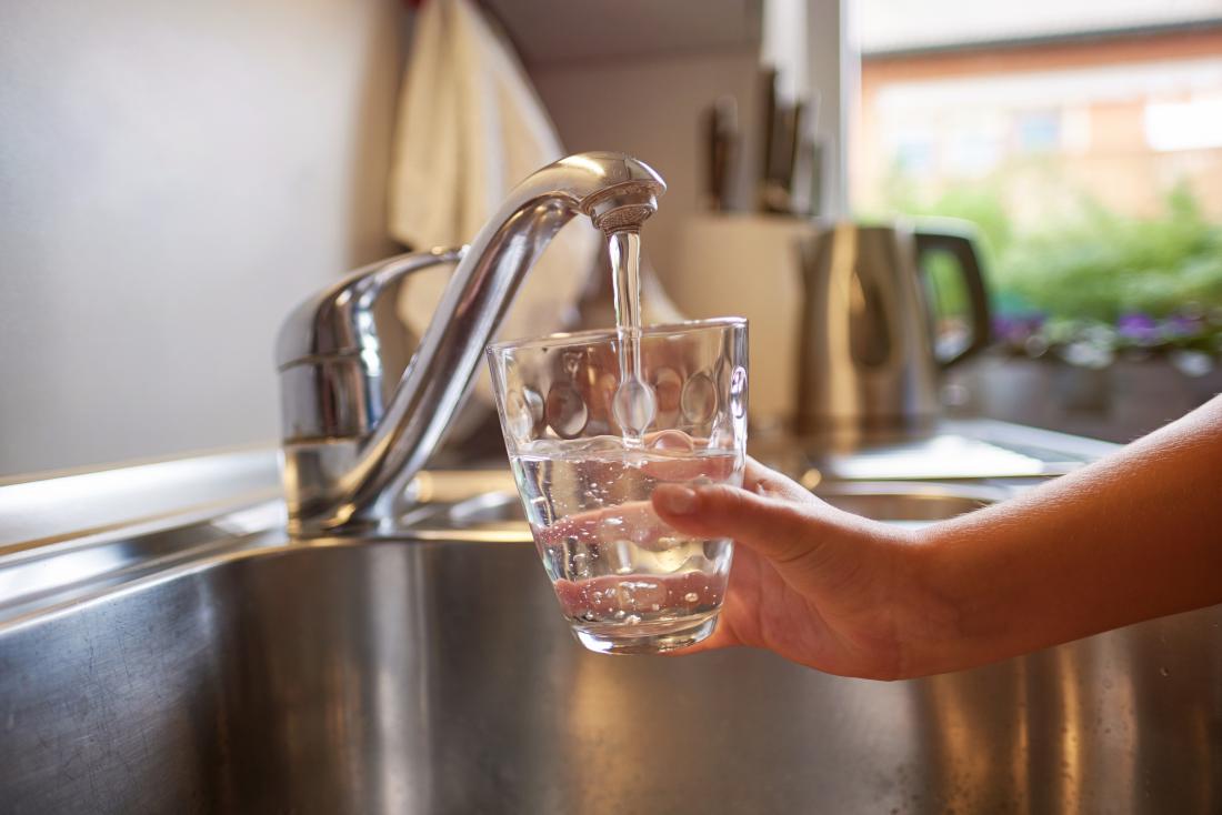 Person pouring water from tap into glass of water for treating cloudy urine