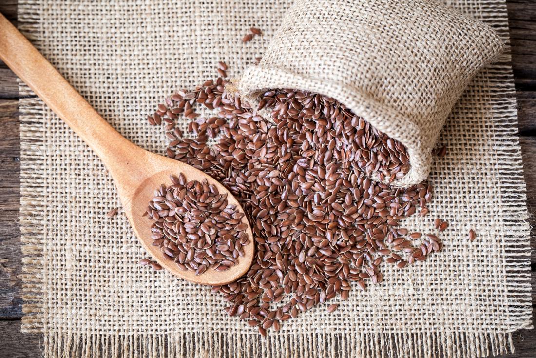 Flax seeds spilling out of sack cloth bag onto wooden spoon