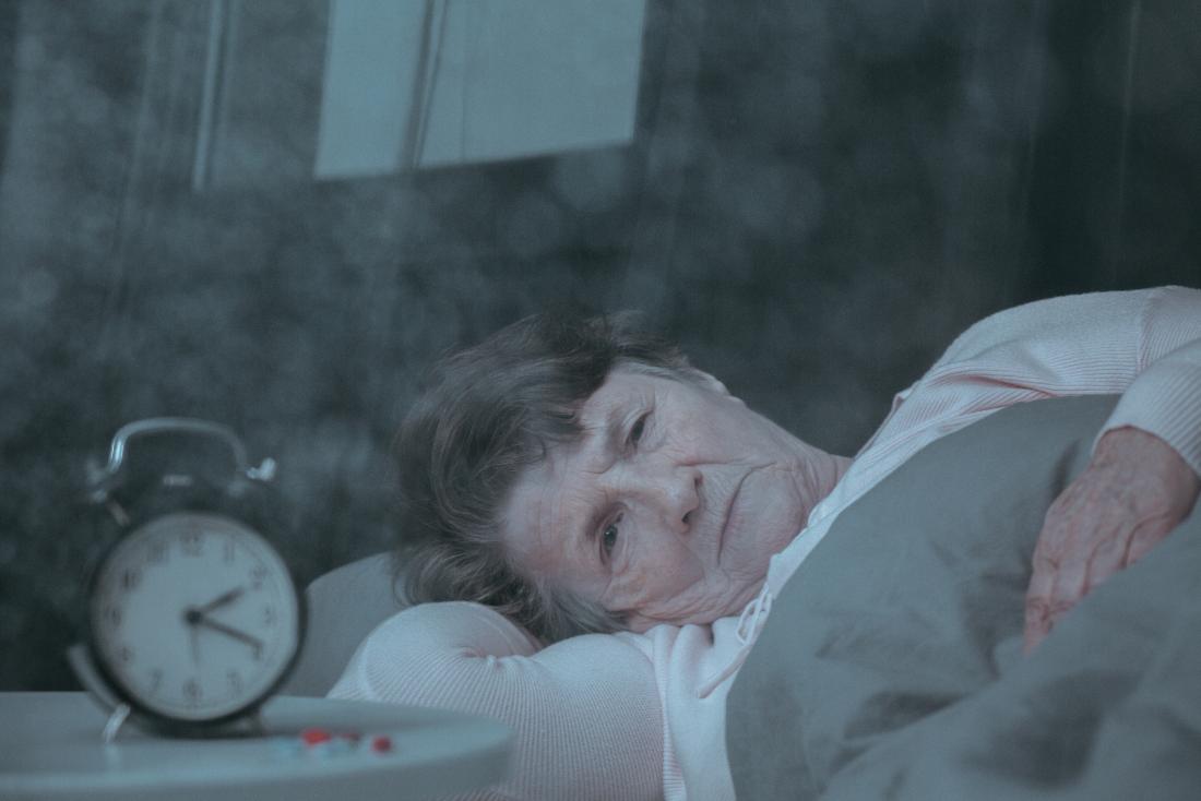 Older women with insomnia due to bipolar disorder lies awake in bed next to alarm clock