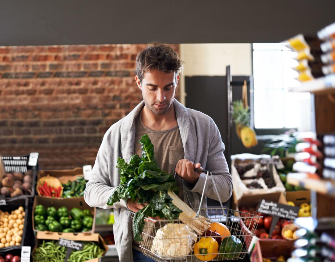 Young man with bipolar stands in grocery store with basket full of vegetables.