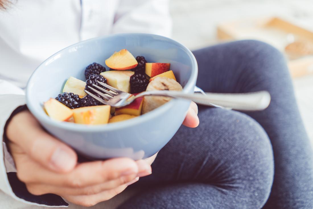 Woman holding bowl of chopped up fresh fruit including apples and blackberries.