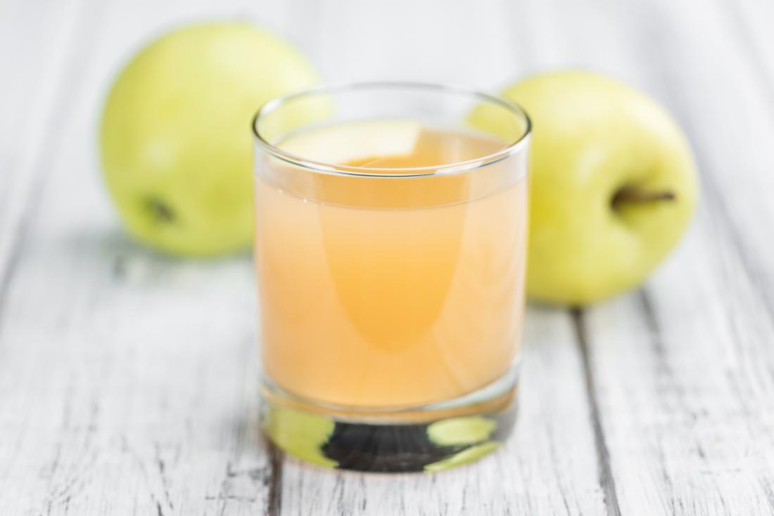 Cloudy apple juice on wooden table with whole green apples in background