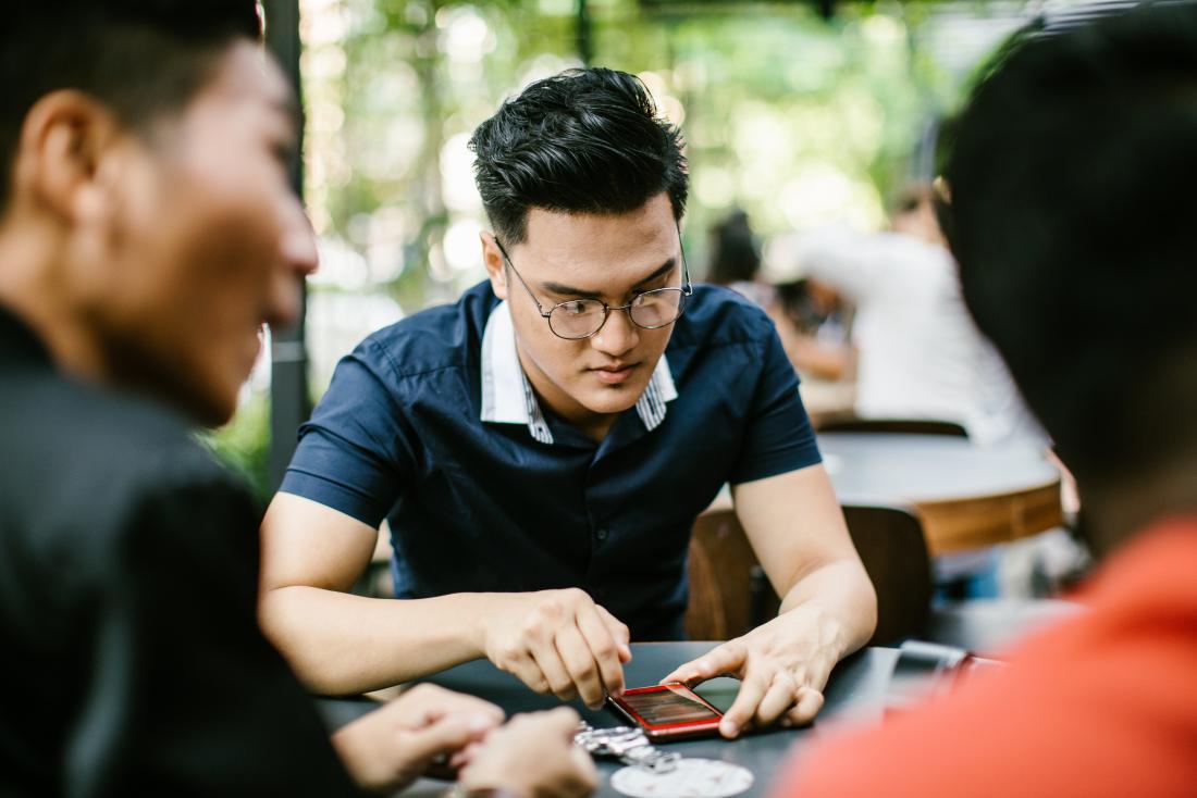 Distracted man with bipolar and adhd playing with smartphone and outdoor cafe with friends