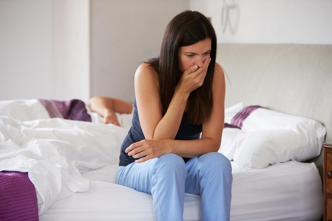 woman sat on the edge of her bed with nausea
