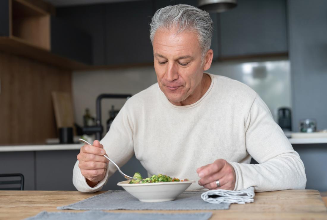 Older man with appetite loss due to bipolar disorder sits alone at table eating a salad.