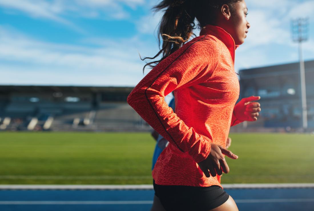 Woman using BCAAs supplement running on racing track.