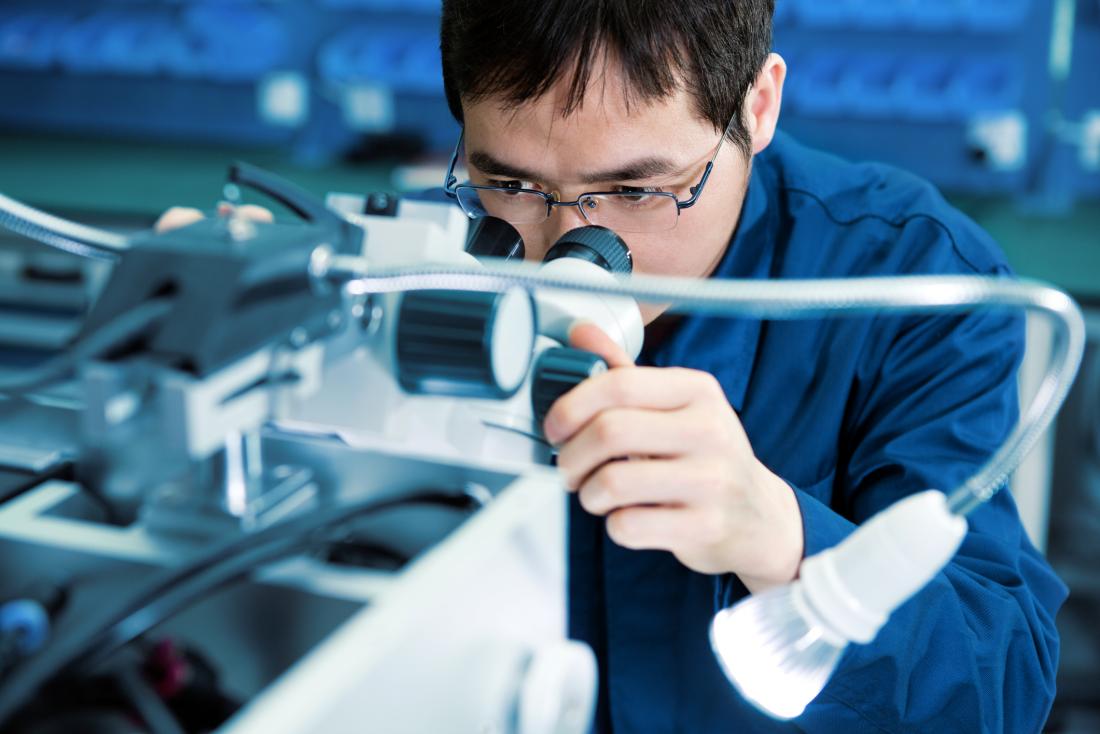 researcher in lab peering through microscope