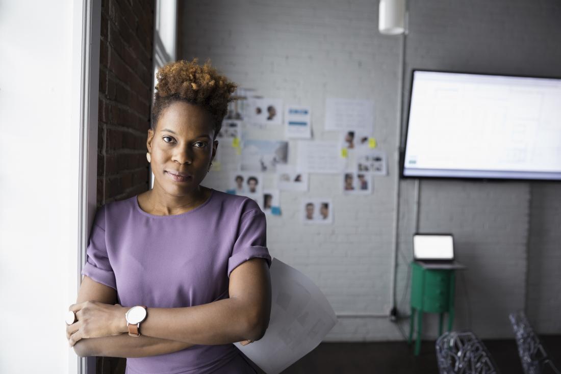 Woman with Crohn's facing camera in business room folded arms.