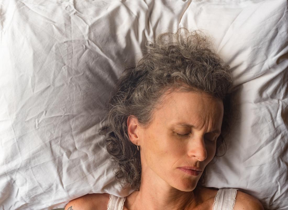 نزدیک یک زن موی خاکستری که روی بالش سفید خوابیده است