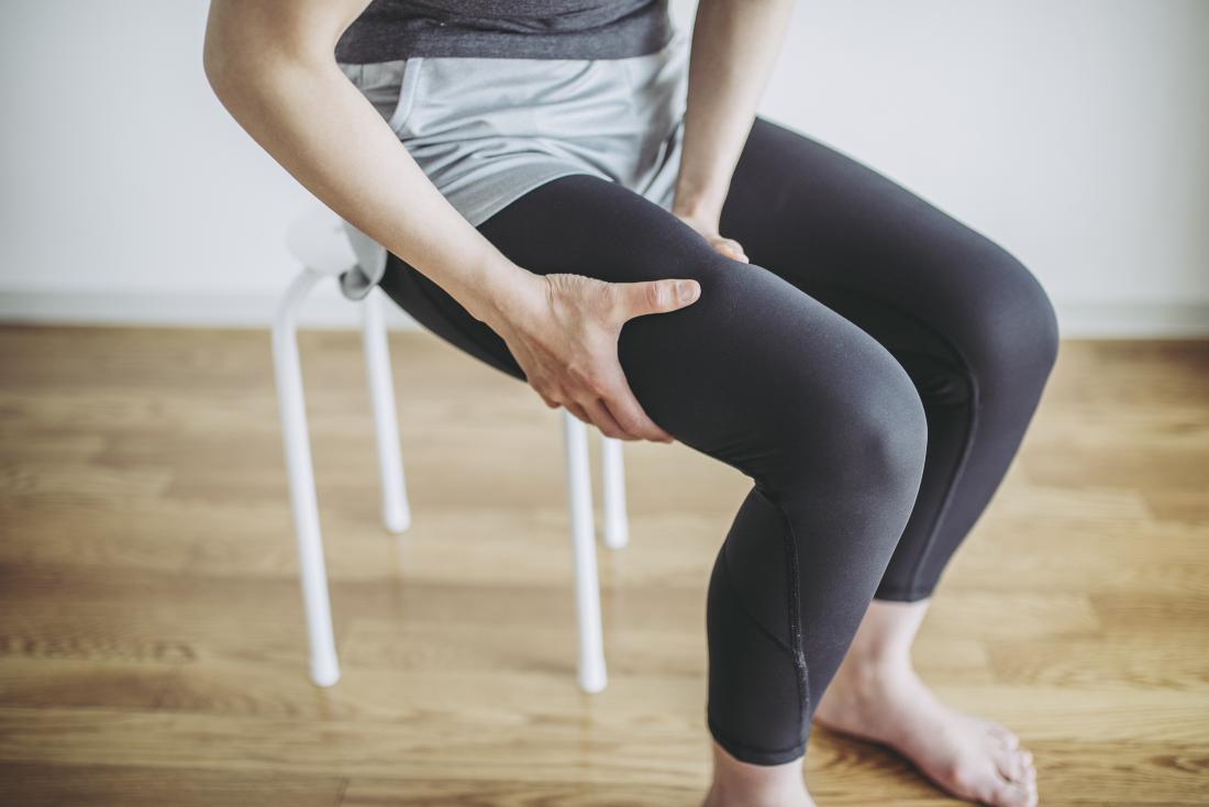 Persona que se sujeta el muslo con dolor debido a las fasciculaciones musculares mientras está sentada en una silla