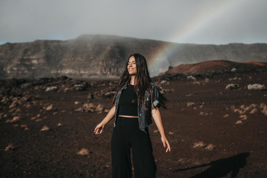 concept photo of smiling woman in a desert with a rainbow behind her