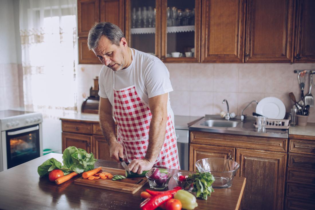 Man wearing apron and chopping vegetables in the kitchen.