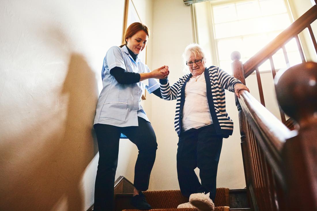 senior woman being helped down the stairs by carer
