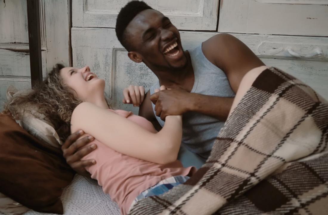 ベッドで笑いながら「生理中に妊娠できますか？」と幸せな若いカップル