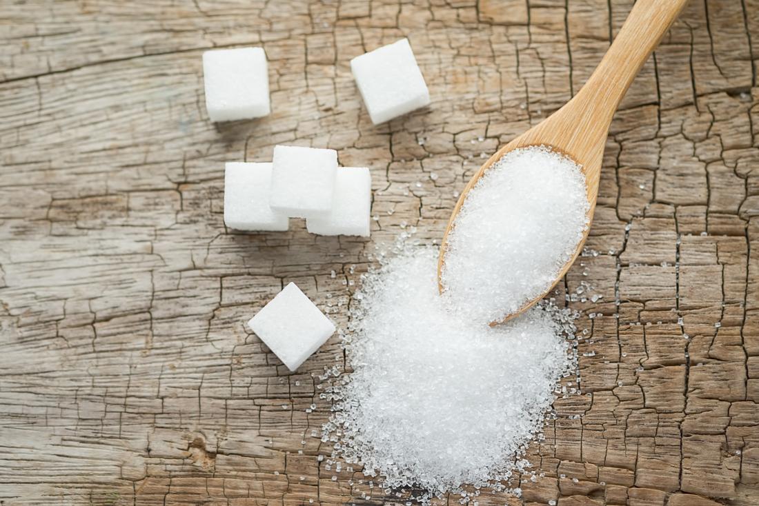 white sugar in wooden spoon on wood grain background