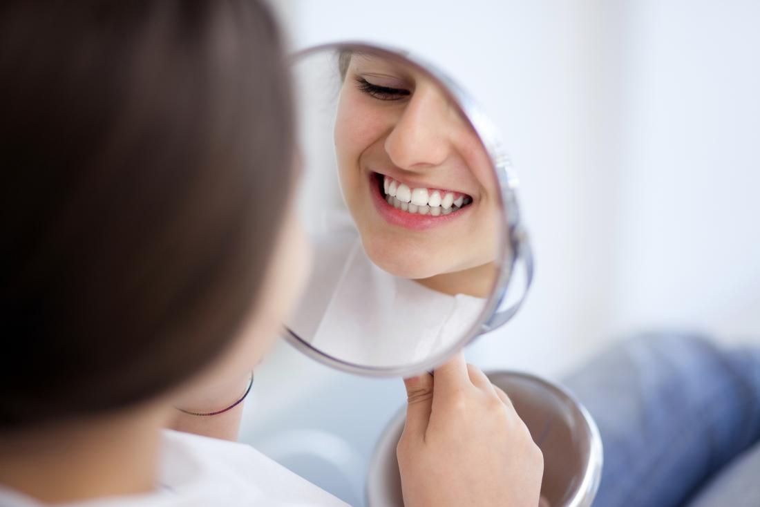 young woman looking at her teeth in mirror