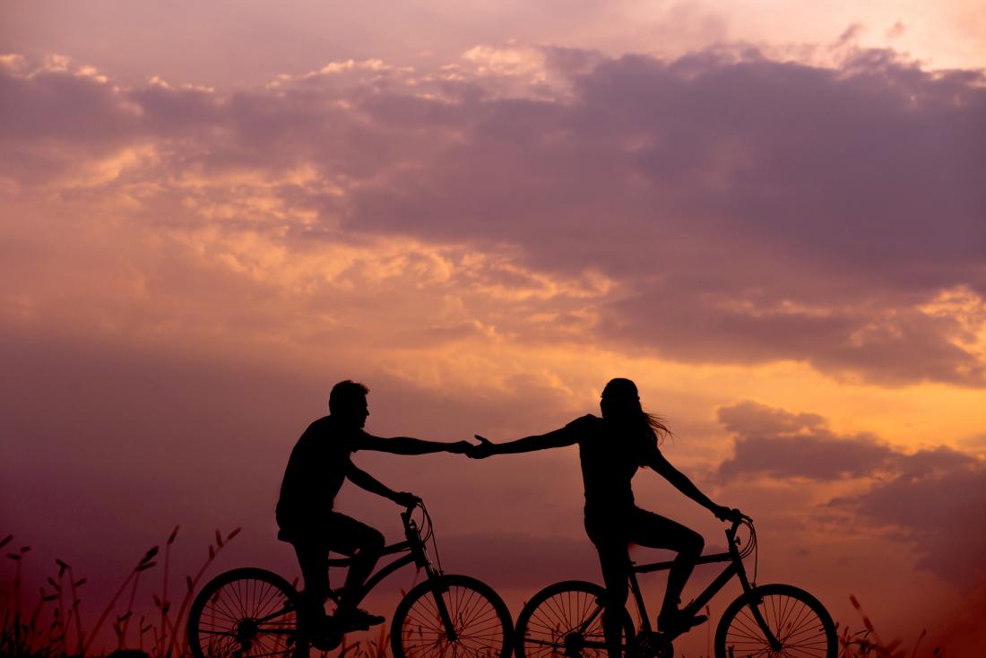 two people on bikes holding hands at twilight