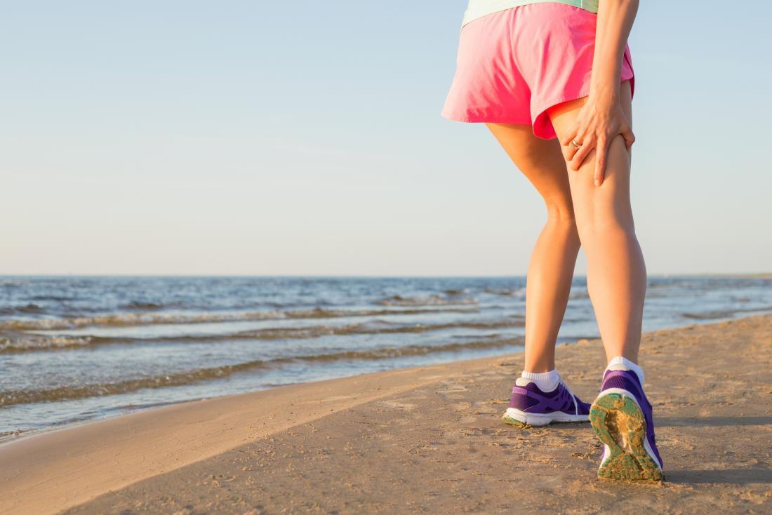 Person with hamstring tendonitis holding back of thigh in pain while running on beach
