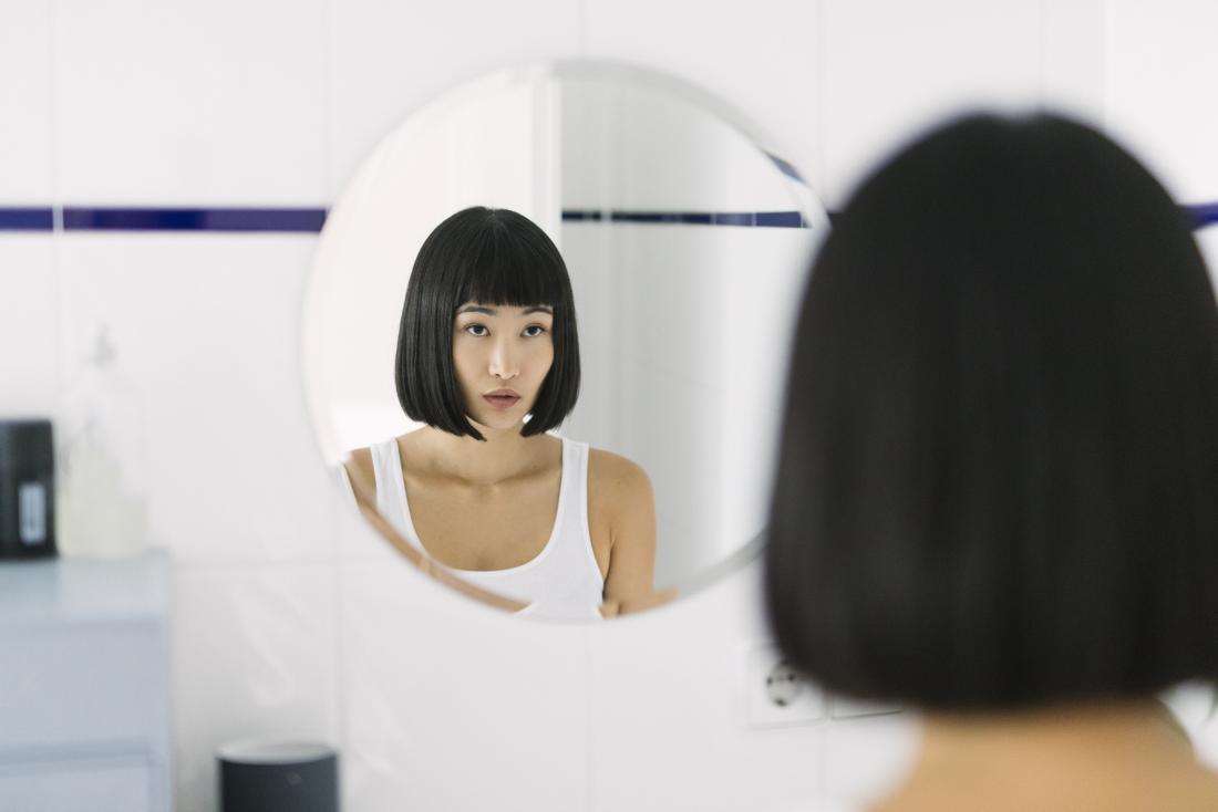 Woman looking in the mirror in the bathroom, slightly concerned about dry nipples