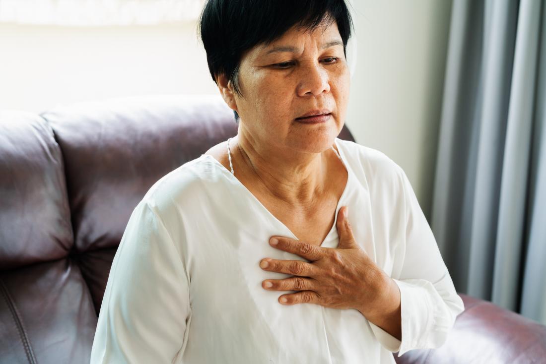 Mature asian woman holding hand to chest due to heart attack or breathing pain.