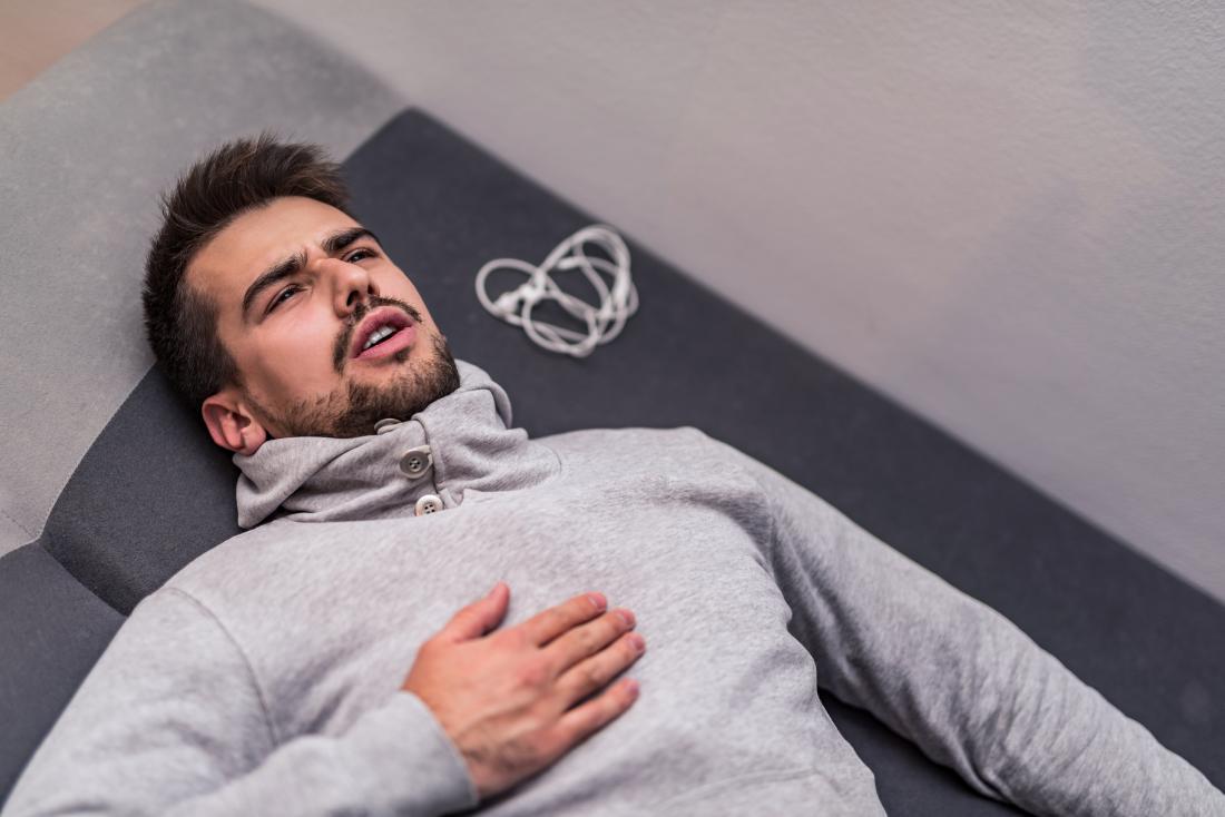 Tired or exhausted man lying down after workout holding chest or abdomen in pain
