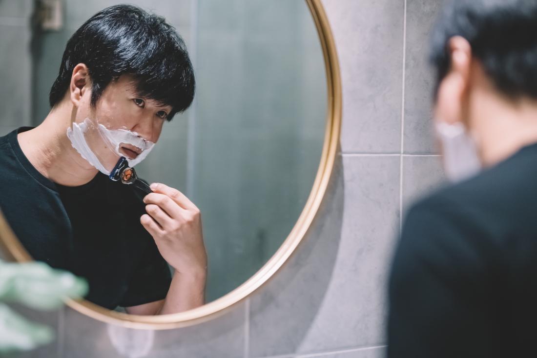 Asian man looking in bathroom mirror shaving