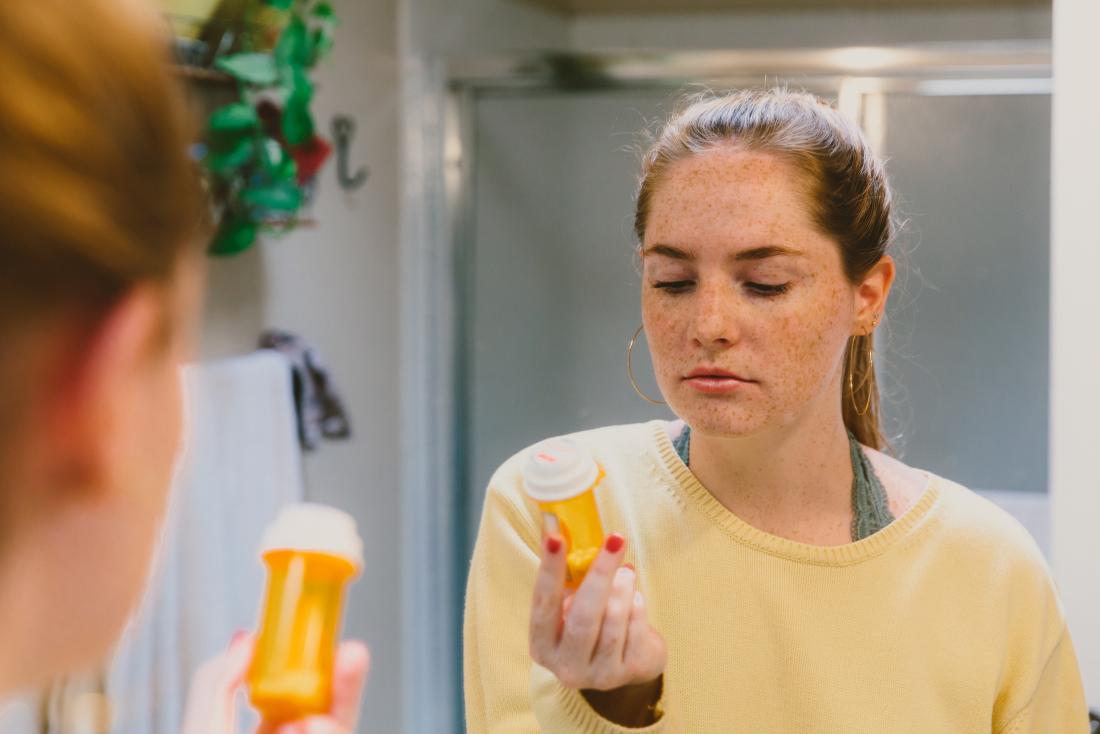young woman reading label on container of mood stabilizers