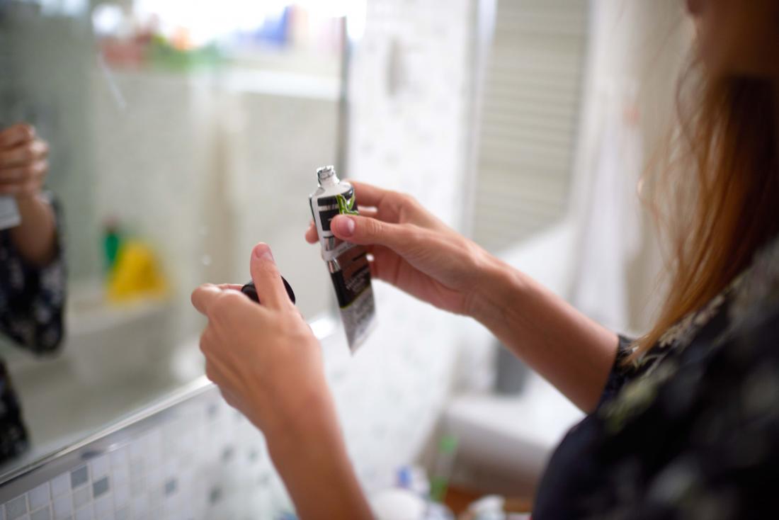 Person in front of bathroom mirror holding tube of skin care product