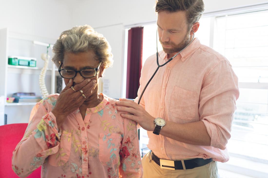 Woman coughing while doctor uses stethoscope to monitor breathing