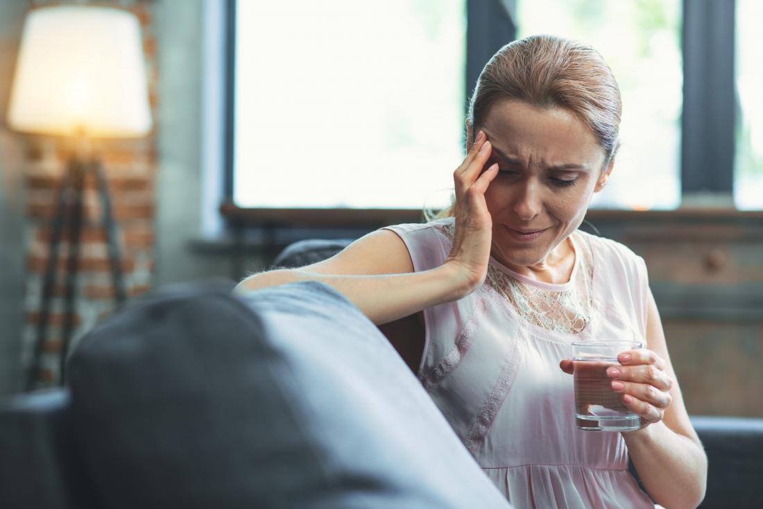 Woman experiencing headache and neuralgia in face holding glass of water in pain