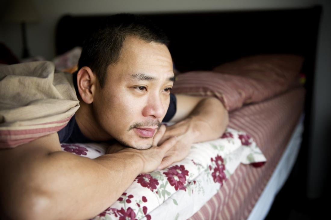 Depressed, sad or lonely man lying on bed under blankets alone.
