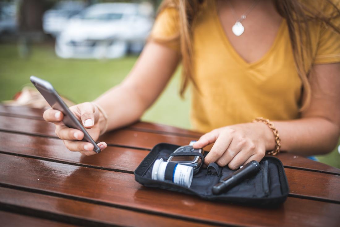 woman checking out her phone while holding blood sugar control kit