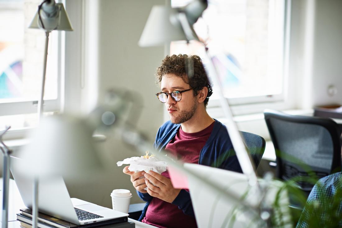 A man eating at his desk. A hidden sign of depression can include appetite and weight changes.