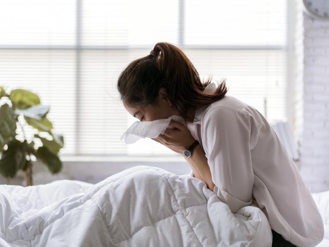 A woman in bed coughing. Symptoms of TB include a bad cough, chest pain, and breathlessness.