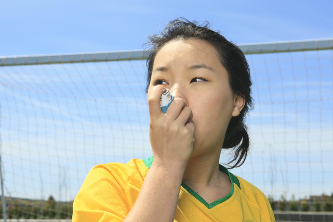 Woman taking inhaler for asthma whilst playing football. Intrinsic and extrinsic asthma have the same symptoms but different triggers