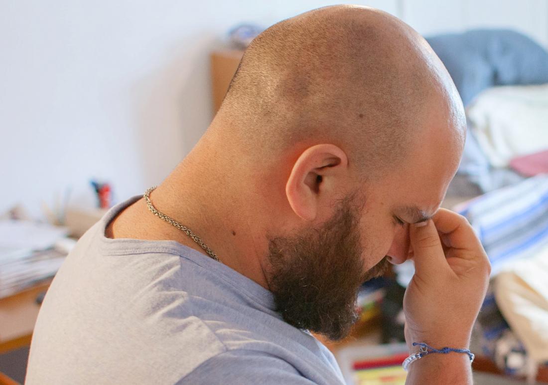 bald man experiencing headache and stress pinching bridge of nose