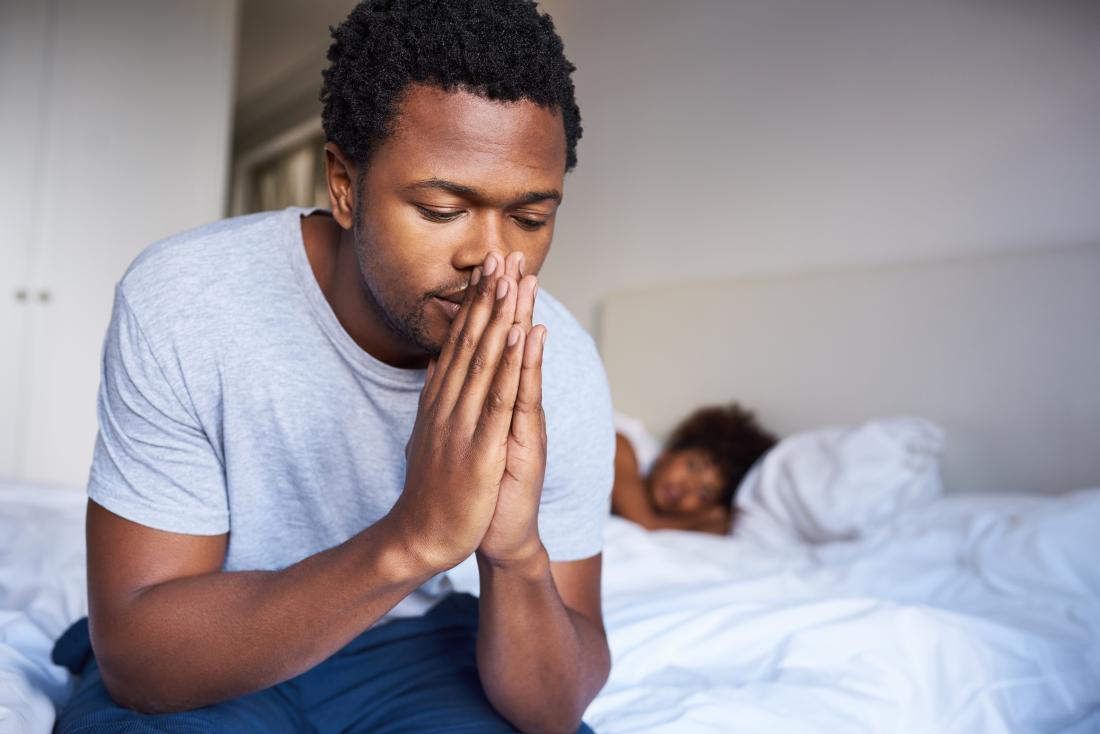 Man looking sad at the side of a bed.