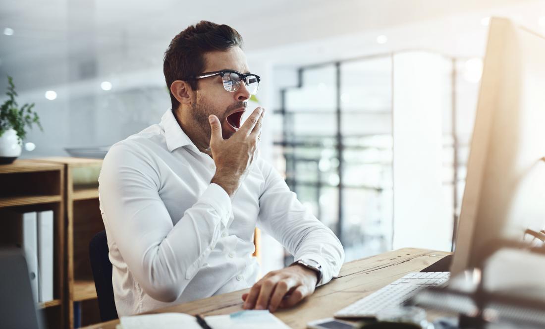 a man at work yawning at his desk.