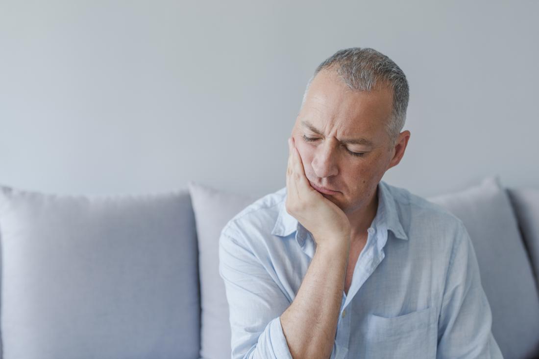 Man with rheumatoid arthritis in jaw holding mouth in pain.