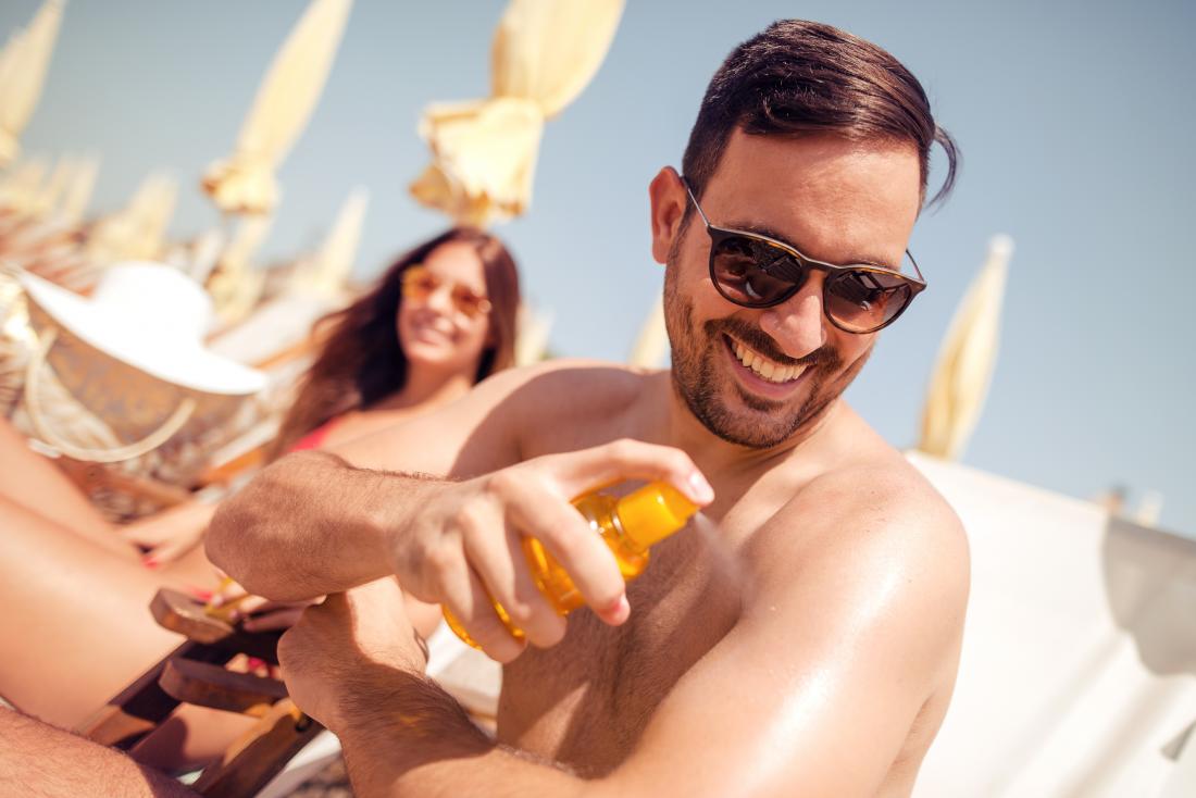 man spraying sun tan lotion on his arm