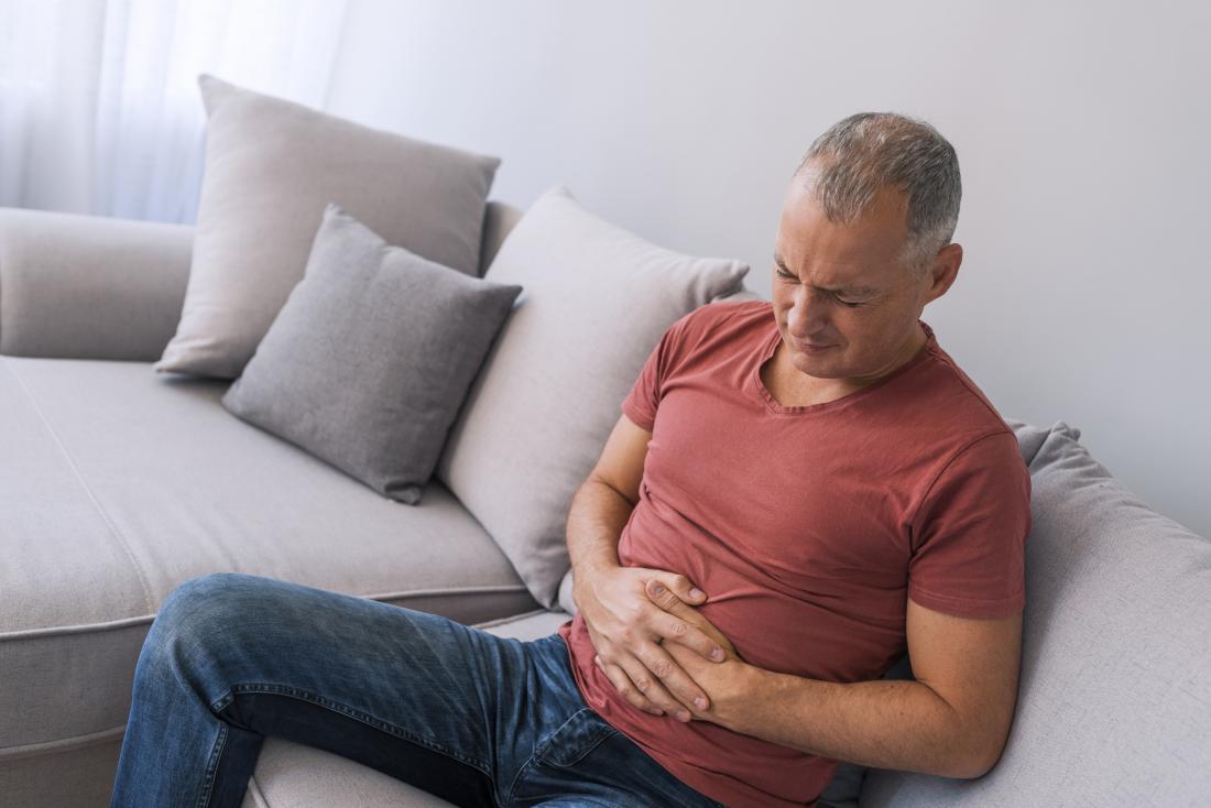 a man getting stomach cramps on his sofa