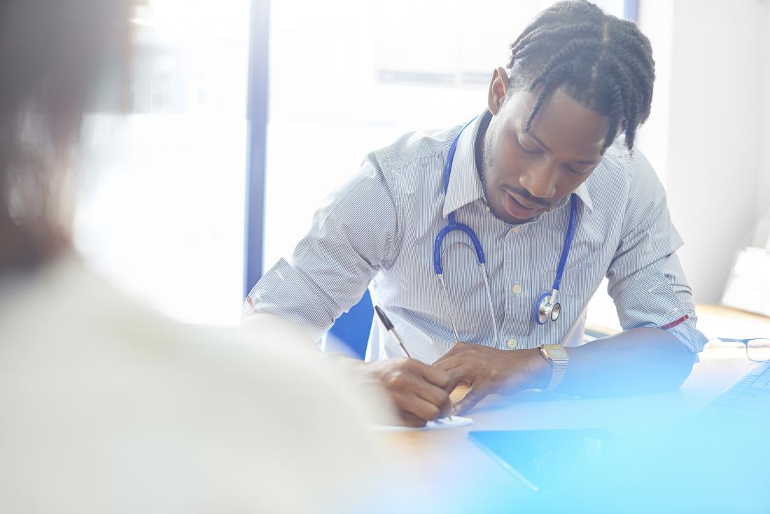 doctor speaking to his patient and writing a prescription