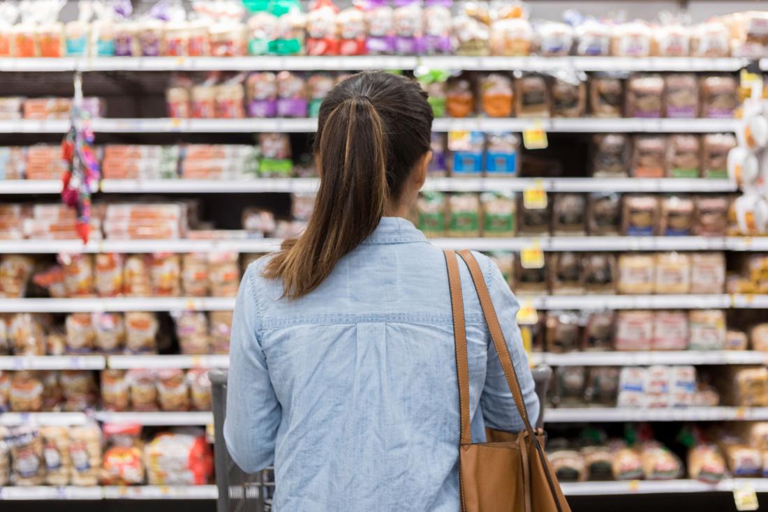 woman looking at processed foods in supermarket aisle seen from behind