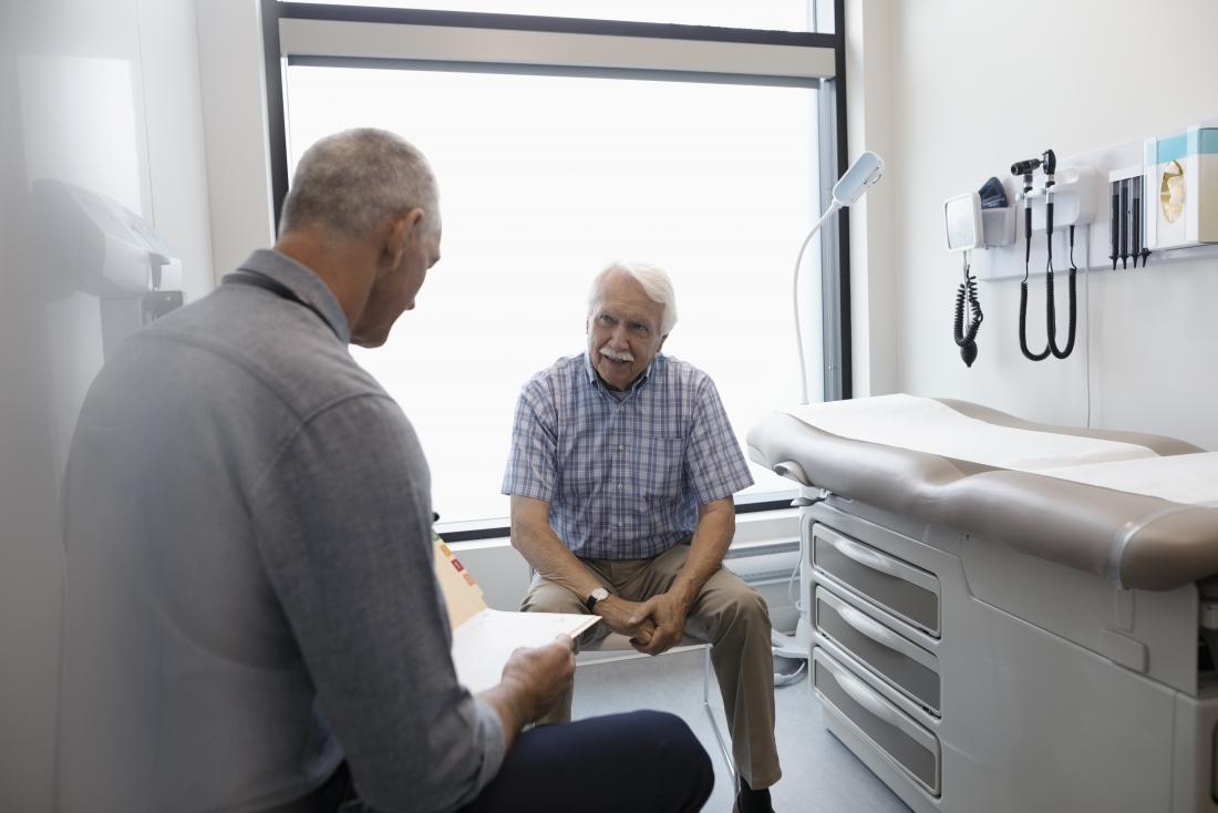 senior man sitting in doctor s office while gp looks at notes
